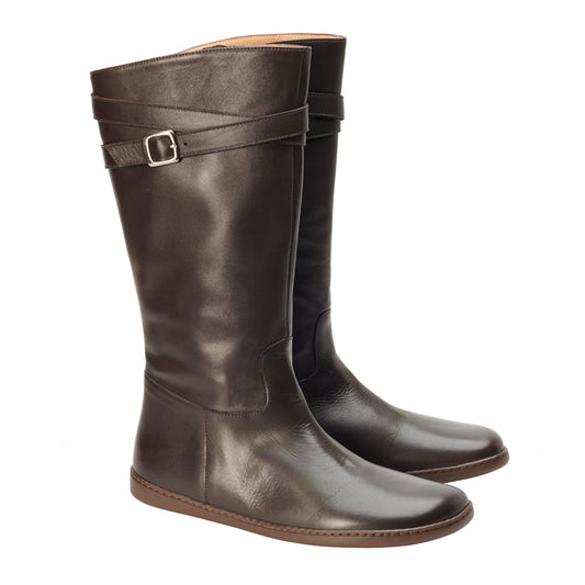 Die ZAQQ ATTRAQT Nappa Brown Stiefel sind hoch und dunkelbraun und zeichnen sich durch ein schlichtes Design mit Riemen und Schnalle oben aus. Sie sind aus glattem Ziegenleder gefertigt, haben flache Sohlen und strahlen bei jedem Schritt Eleganz aus.