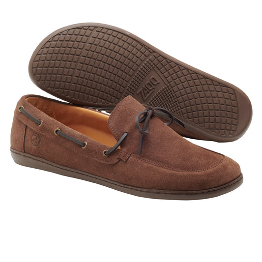 Die Loafer QEA Velours Brown von ZAQQ mit Lederschnürsenkeln und strukturierter Gummisohle werden ausgestellt. Ein Schuh steht aufrecht, während der andere angewinkelt ist, um die Sohle hervorzuheben. Mit Barfußschuheigenschaften für mehr Komfort weisen diese Schuhe Nähte und ein kleines Logo an der Seite auf.