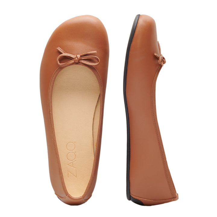 Das Paar brauner Ballerinas ist aus LOOQ Vegan Cognac-Material gefertigt und hat vorne eine kleine Schleife. Ein Schuh ist von oben und der andere von der Seite zu sehen, wodurch die glatte Oberfläche und die runde Spitze zur Geltung kommen. Die Innensohle ist mit dem ZAQQ-Logo versehen und sie verfügen über eine Barfußsohle für ultimativen Komfort.