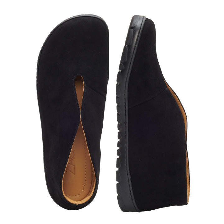 Ein Paar TSEQA Slipper aus schwarzem Wildleder von ZAQQ weist eine sichtbare hellbraune Innenseite auf. Das Design zeigt einen Schuh von oben und den anderen von der Seite, wodurch die dicke OUTDOOR-Sohle und die markante V-förmige Öffnung im oberen Bereich hervorgehoben werden.