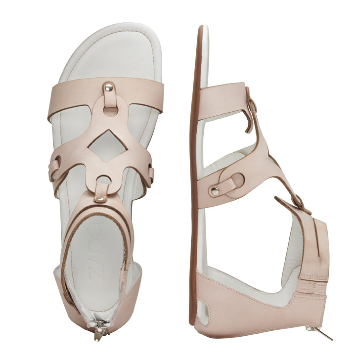 Die MAROQ Nude von ZAQQ ist eine beige Barfußsandale aus Nappaleder mit offener Spitze, Knöchelriemen und eleganten Cut-Out-Details. Diese Sandalen haben sichere Schnallenverschlüsse und sind mit einer strapazierfähigen Kautschuksohle versehen. Eine Sandale ist von oben zu sehen, während die andere von der Seite zu sehen ist.