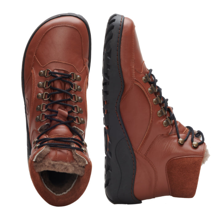 Ein Paar ZAQQ TERRAQ Cognac Winter Waterproof Wanderstiefel aus braunem Nappaleder mit schwarzen Schnürsenkeln, Metallösen und einem Plüschfutter. Die sichtbaren, robusten schwarzen Gummisohlen unterstreichen das stilvolle Design, da ein Stiefel aufrecht steht und der andere auf der Seite liegt, sodass die Sohle sichtbar ist. Diese Stiefel sind perfekt für ein modisches Winterabenteuer.