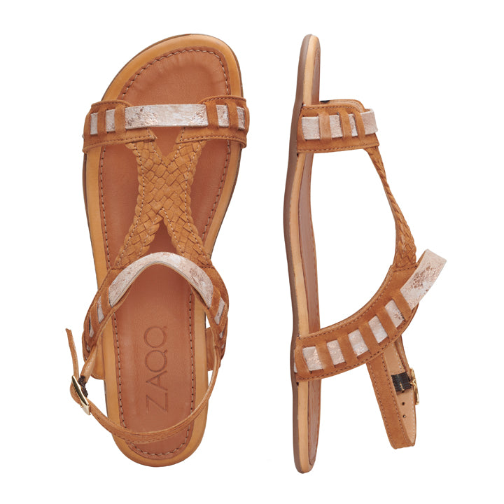 Die BLINQ Brown Sandalen von ZAQQ zeigen mit ihrem hellbraunen und weißen Riemchenlook ein feminines Design. Eine Sandale ist horizontal positioniert, um das gewebte Riemendetail hervorzuheben, während die andere vertikal steht und die Aufmerksamkeit auf den offenen Zehenbereich und den verstellbaren Schnallenverschluss lenkt. Die Innensohle trägt deutlich den Markennamen ZAQQ, was sie zu einer idealen Wahl für schicke Barfußsandalen macht.