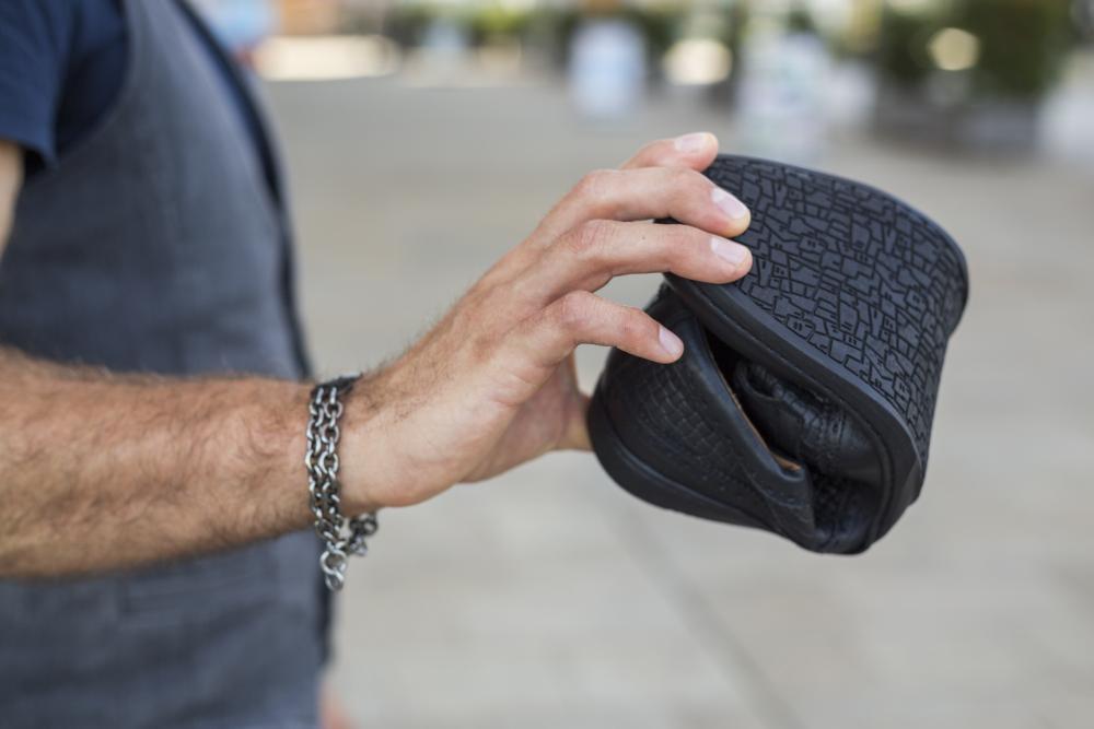 Eine Person mit einem Kettenarmband hält im Freien ein ZAQQ BRIQ Brogue Tresse Black Virtual Reality-Headset. Der Arm der Person ist sichtbar, wodurch die Details ihrer Hand und ihres Handgelenks hervorgehoben werden, während der Hintergrund leicht unscharf bleibt.