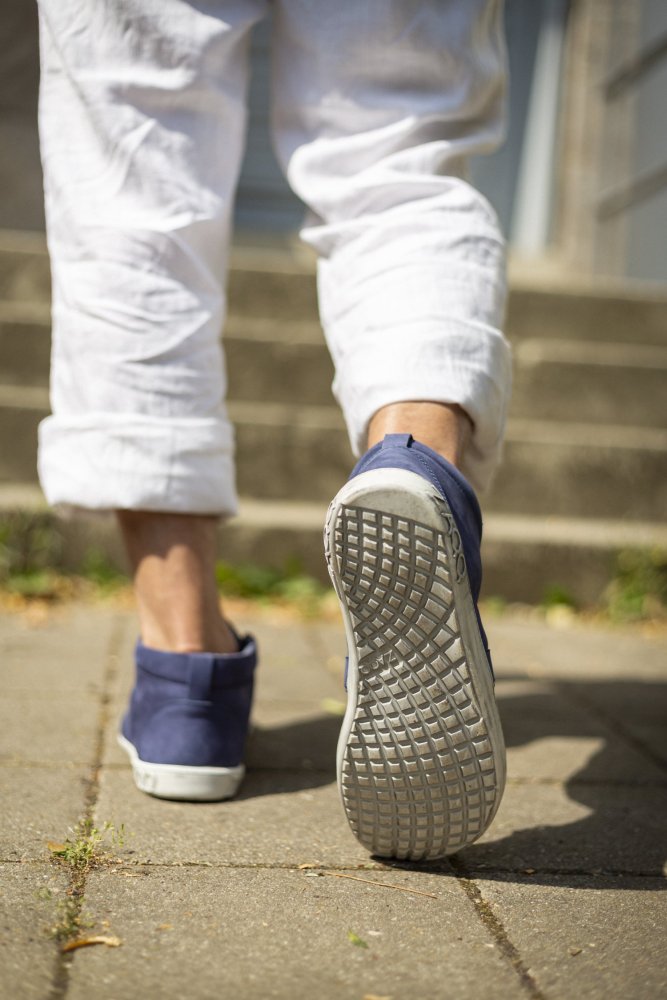 Eine Person in weißen Hosen und eleganten Schuhen von ZAQQ LANQASTER Navy geht im Freien die Betonstufen hinauf, wobei der Fokus auf ihren Schuhen und dem strukturierten Bürgersteig liegt.