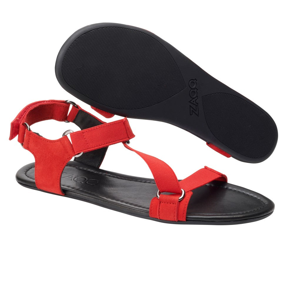 Ein Paar MIQA Red-Sandalen von ZAQQ mit schwarzer Sohle. Die Barfußsandale verfügt über verstellbare Knöchelriemen mit Metallringen und wird mit einer Sohle nach oben präsentiert, die einen strukturierten Griff für zusätzliche Stabilität bietet.