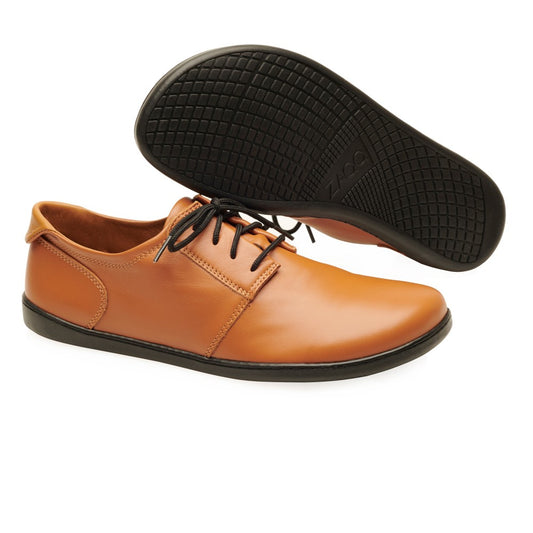 Diese eleganten braunen Lederschuhe von ZAQQ aus PIQUANT Nappa Cognac haben schwarze Schnürsenkel und strukturierte Sohlen. Ein Schuh ist kunstvoll positioniert, um sein kompliziertes Design zur Geltung zu bringen.