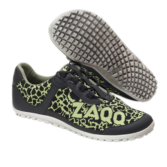 Wir präsentieren den QASEY Green von ZAQQ: ein Paar Freizeitschuhe mit einem auffälligen schwarz-grünen Musterdesign aus veganen Materialien. Die Schuhe zeigen das ZAQQ-Logo deutlich sichtbar an der Seite. Sie sind mit einer klassischen weißen Sohle mit Barfußschuhstruktur für besseren Halt ausgestattet. Ein Schuh ist aufrecht stehend abgebildet, während der andere auf der Seite liegt, um das einzigartige Sohlendesign zu präsentieren.