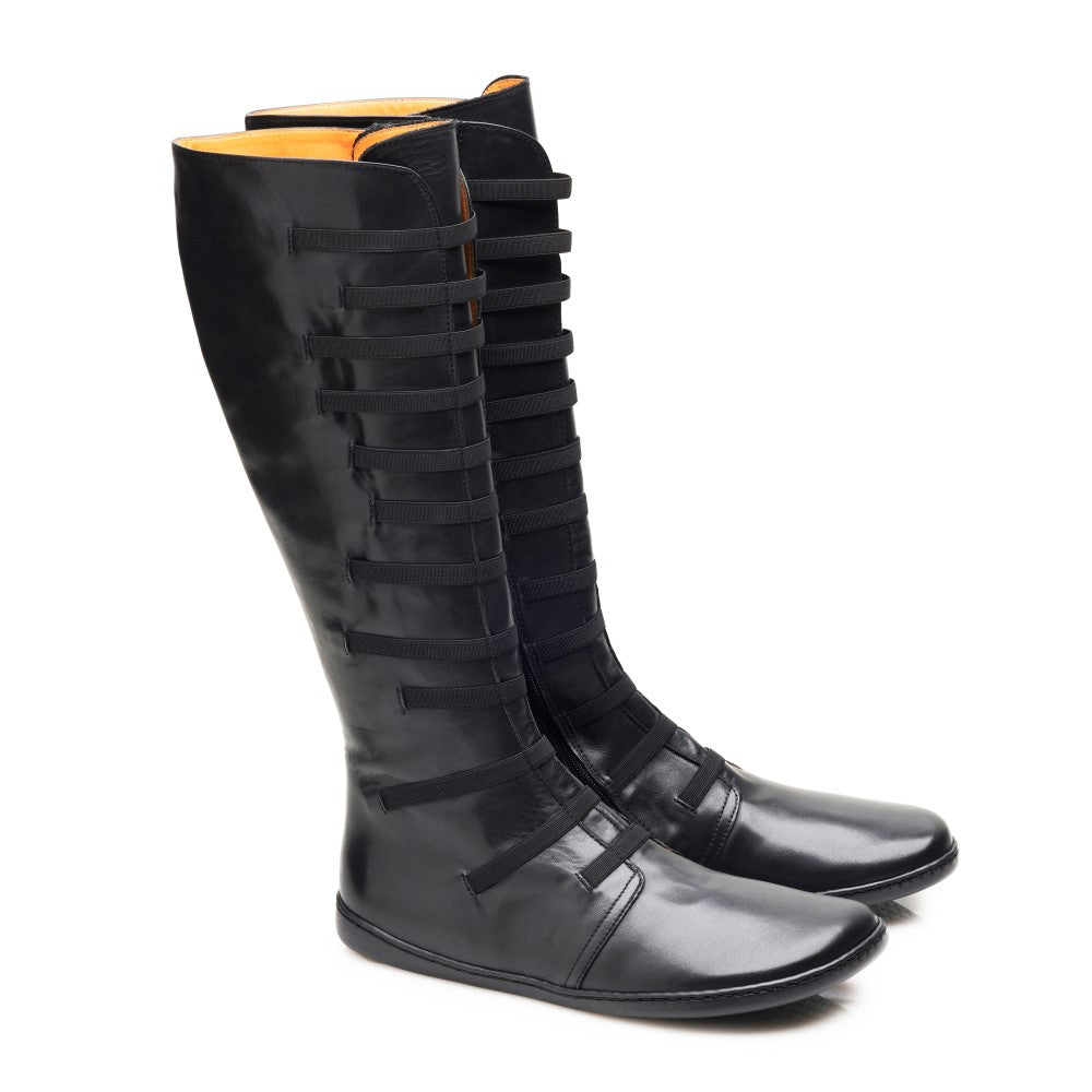 Die kniehohen Stiefel QATCH Stretch Nappa Black von ZAQQ mit einzigartigem Riemchendesign und flacher Gummisohle werden vor einem weißen Hintergrund präsentiert.