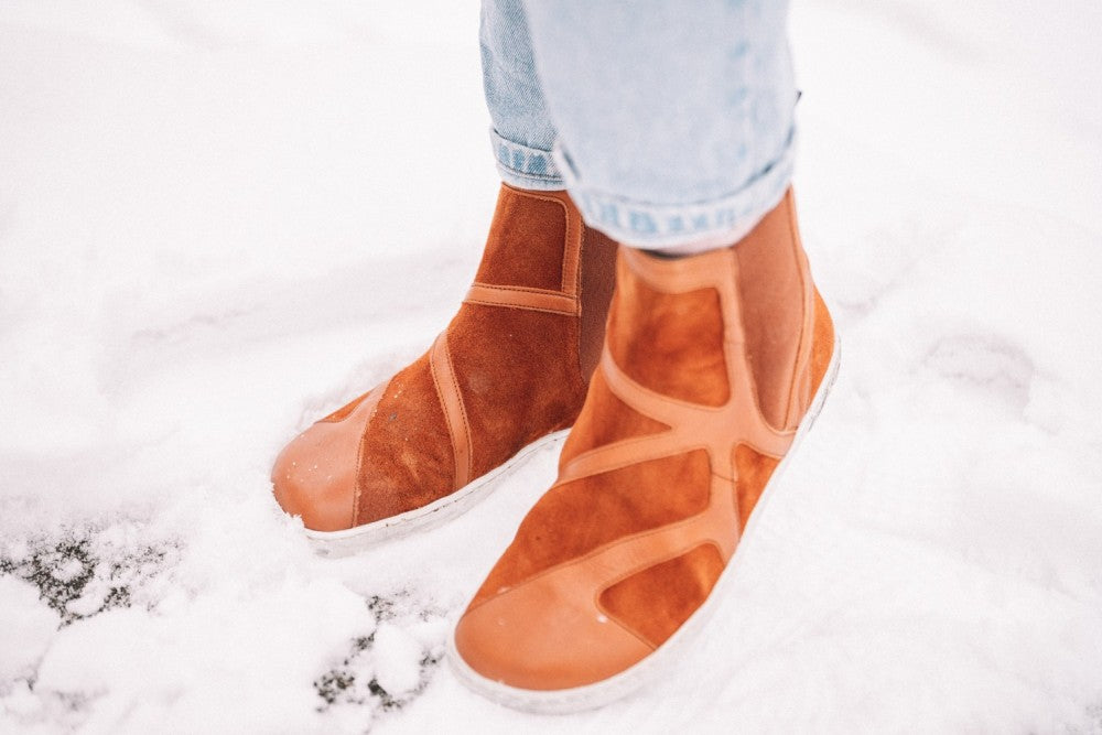 Eine Person in den Cognac-Leder- und Wildlederstiefeln „QEY WEST“ von ZAQQ steht im Schnee. Die Unterteile ihrer hellblauen Jeans sind sichtbar.