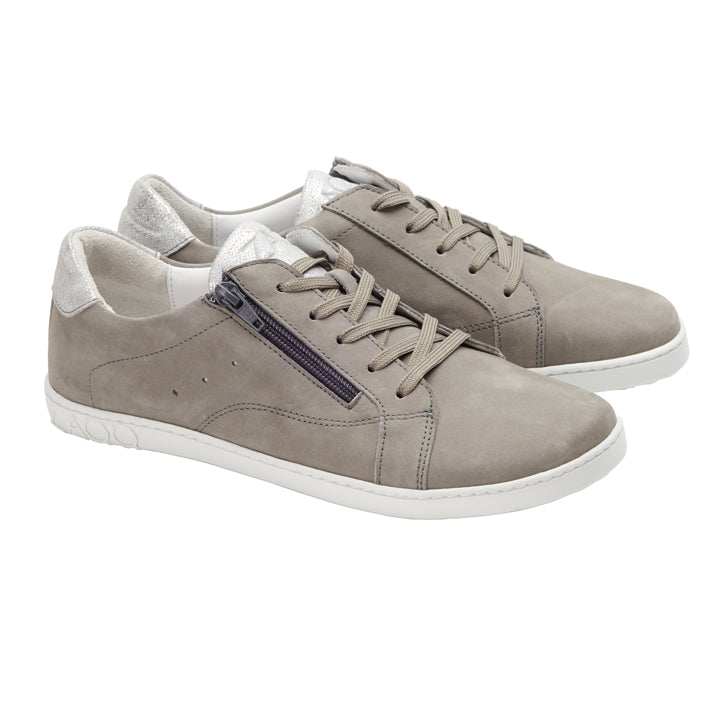 Wir präsentieren die QOMFY Wide Grey Sneaker von ZAQQ: ein stilvolles Paar grauer Freizeit-Sneaker aus Veloursleder. Sie haben weiße Sohlen und beige Schnürsenkel, Reißverschlussdetails an der Seite und einen silbernen Metallic-Akzent an der Ferse für zusätzliches Flair. Erleben Sie bei jedem Schritt ultimativen Komfort.