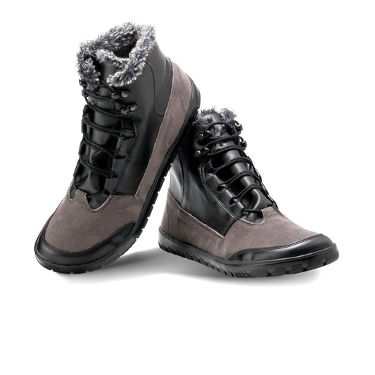 Ein Paar stylische, wasserdichte Winterstiefel namens QUEST Black Waterproof von ZAQQ, gestaltet mit dunklem Leder und grauen Wildledereinsätzen. Diese Outdoor-Schuhe verfügen über ein kuscheliges Fellfutter an der Oberseite und sind mit robusten schwarzen Schnürsenkeln ausgestattet, ergänzt durch eine robuste Sohle für optimale Traktion. Ein Stiefel ist leicht geneigt, um sowohl die Vorder- als auch die Seitenansicht zu präsentieren.