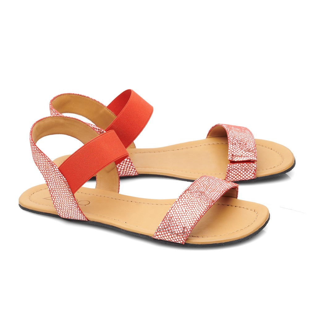 Die SLIQ-Red von ZAQQ sind ein Paar stylische flache Sandalen aus Nappaleder mit hellbrauner Sohle, roten Knöchelriemen und weiß gemusterten Vorderriemen. Diese Barfuß-Sandalen bieten mit ihrem offenen Zehendesign außergewöhnlichen Tragekomfort und sind elegant auf weißem Hintergrund gestaltet.