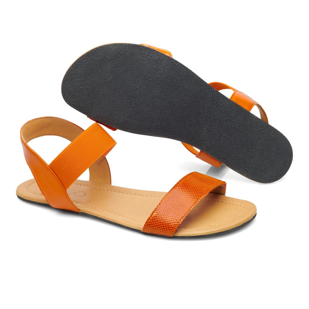 Die SLIQ-Orange Sandalen von ZAQQ bieten eine modische Kombination, bei der eine Sandale von oben gezeigt wird und die andere ihre schwarze Sohle betont. Der Barfußsandale-Stil umfasst einen einzelnen Riemen über den Zehen, gepaart mit einem eleganten Knöchelriemen, was sowohl Komfort als auch Eleganz bietet.