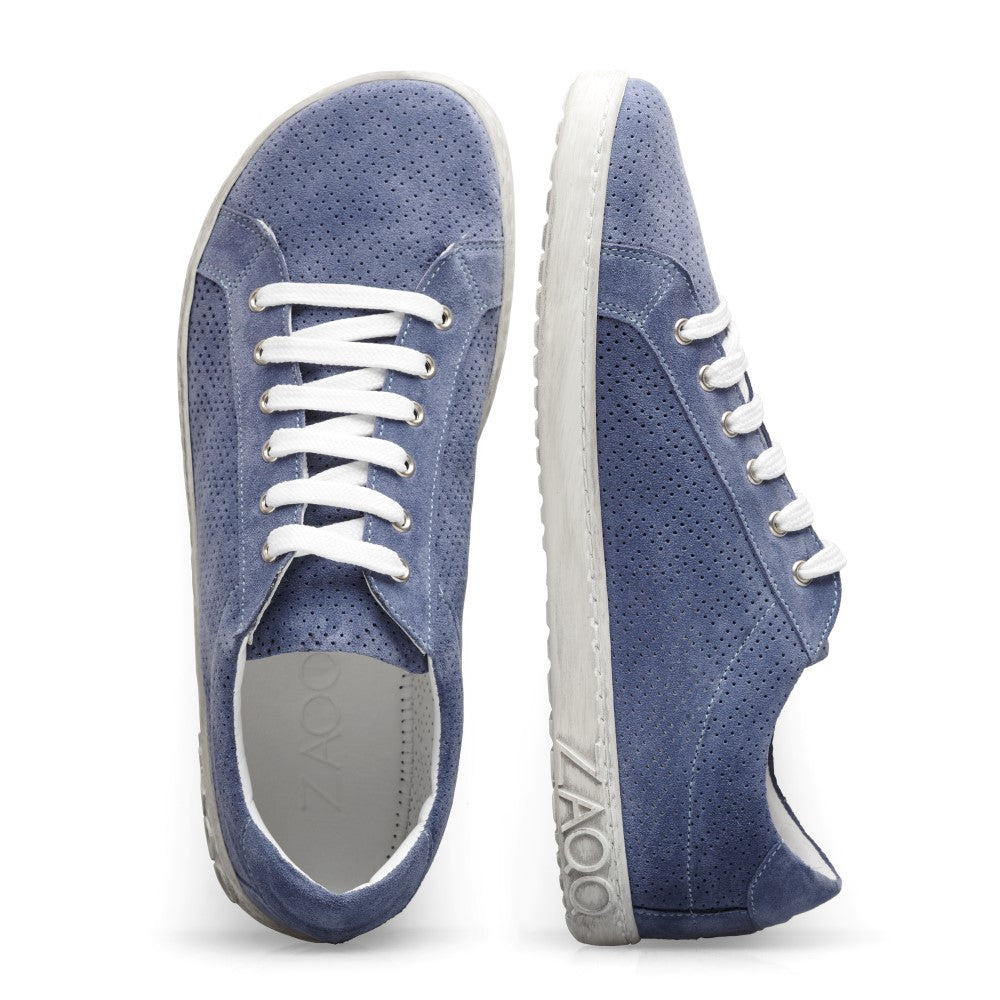 Ein Paar SLOQ Blue Sneaker von ZAQQ aus blauem Veloursleder mit auffälligen weißen Schnürsenkeln und Sohlen, mit perforiertem Design und dem Logo der Marke an der Seite. Ein Sneaker steht aufrecht, während der andere auf der Seite liegt.