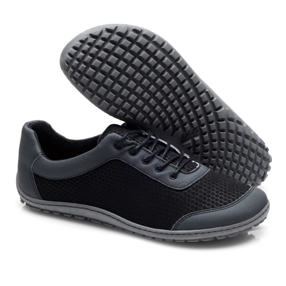 Wir präsentieren die SQIP Black Grey Sneaker von ZAQQ: Diese stylischen Schuhe sind aus schwarzem veganem Leder gefertigt und haben graue Sohlen und Schnürsenkel sowie eine strukturierte Oberfläche. Ein Sneaker steht aufrecht, während der andere auf der Seite liegt, wodurch das Profilmuster der Sohle hervorgehoben wird. Sie bieten hohen Tragekomfort und sind somit perfekt für den Alltag.